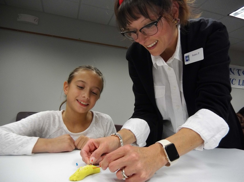 Ms. Robin helps Sarah make a circuit with play-dough, clay and two light-emitting diodes.